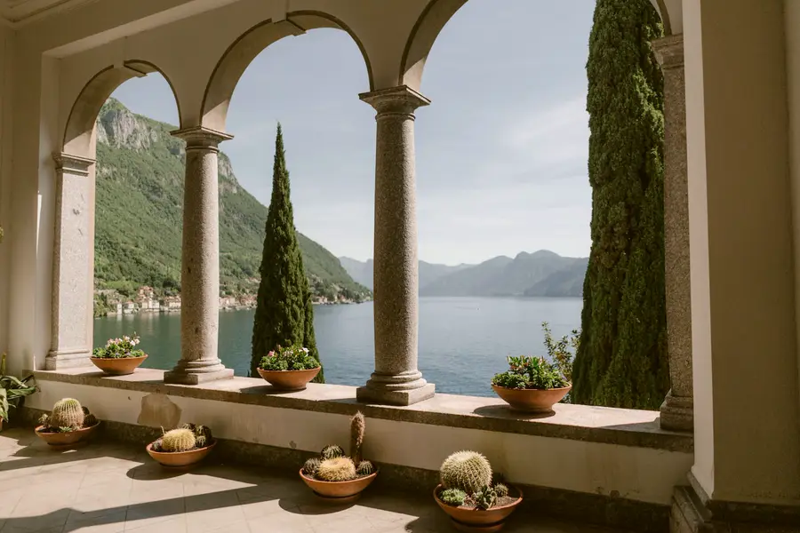 A stone loggia with cypress and potted cacti looking out over Lake Como.