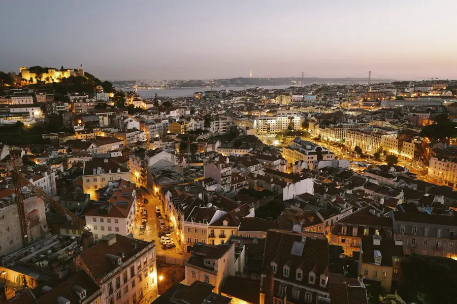 Lisbon’s rooftops and lamplit streets descending toward the Tagus at dusk.